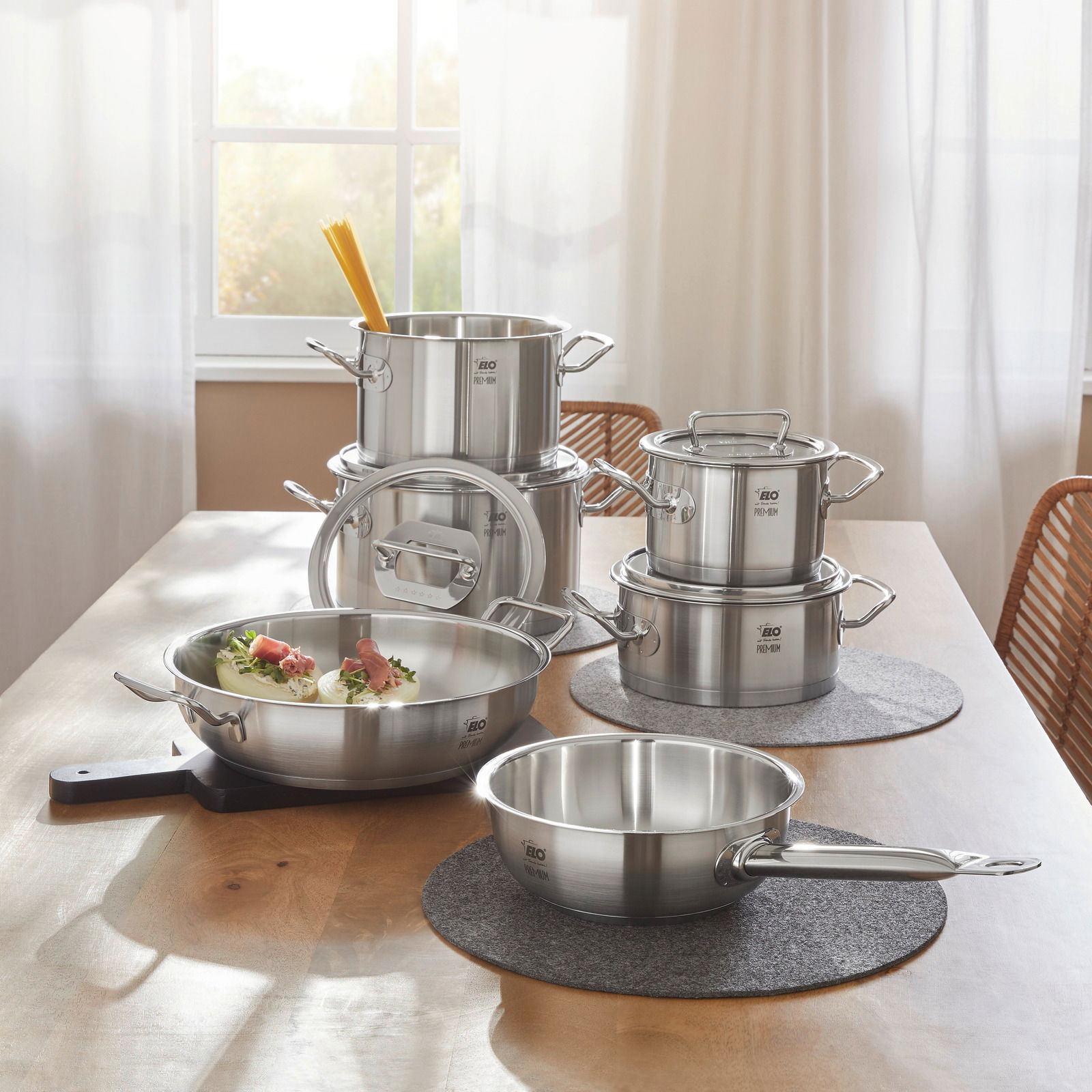 Topfset Gourmet Plus 6-tlg. aus Edelstahl, bestehend aus mehreren Töpfen und Pfannen, auf einem Tisch in einer hellen Küche präsentiert. Perspektive von vorne.