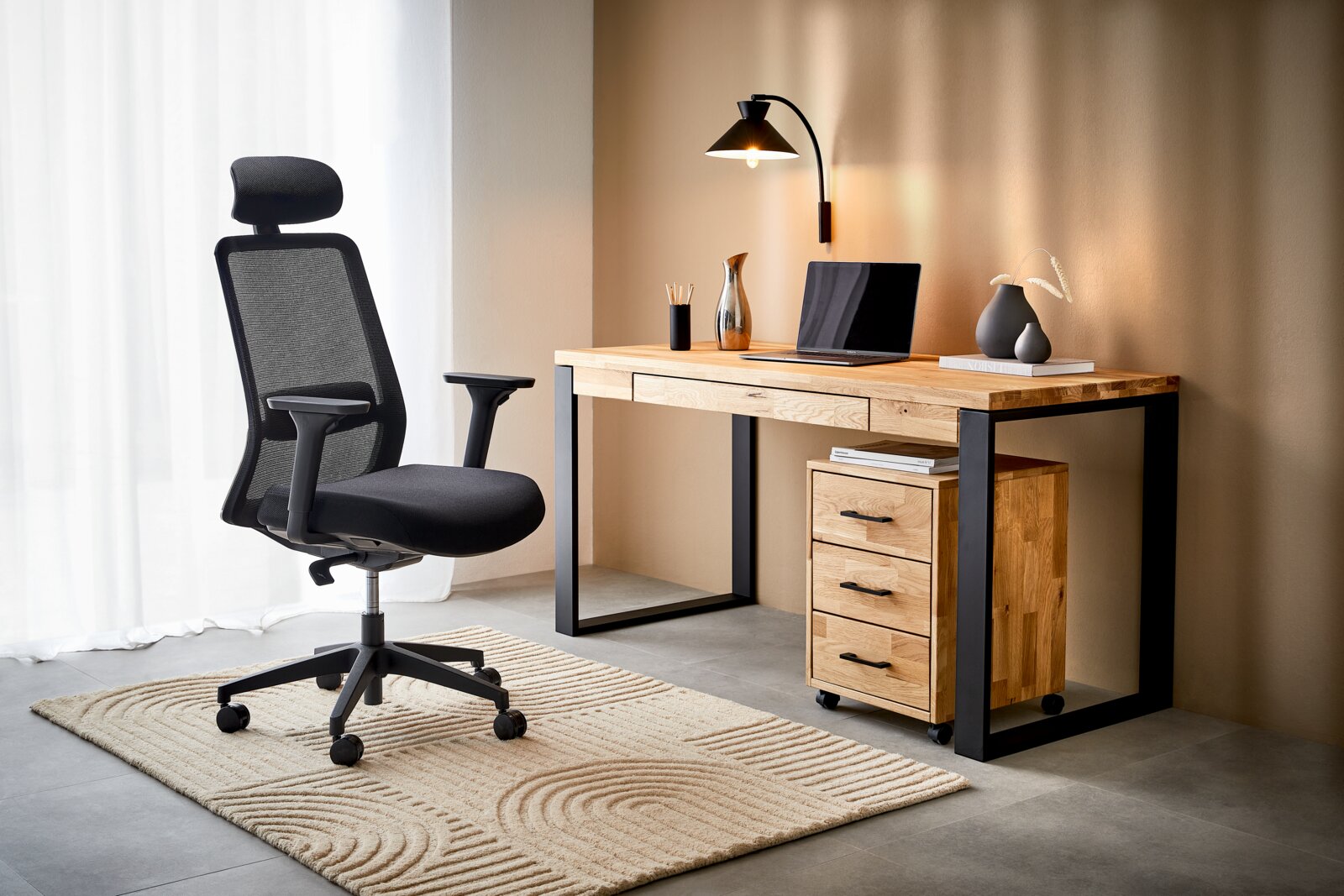 Moderner Schreibtisch aus Holz mit schwarzem Metallrahmen, seitlich mit Schubladen, von vorne betrachtet. Daneben steht ein ergonomischer Bürostuhl auf einem Teppich.