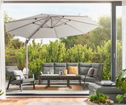 Gartenlounge-Set mit grauen Polstern und einem großen Sonnenschirm, aus der Perspektive einer offenen Terrassentür fotografiert.