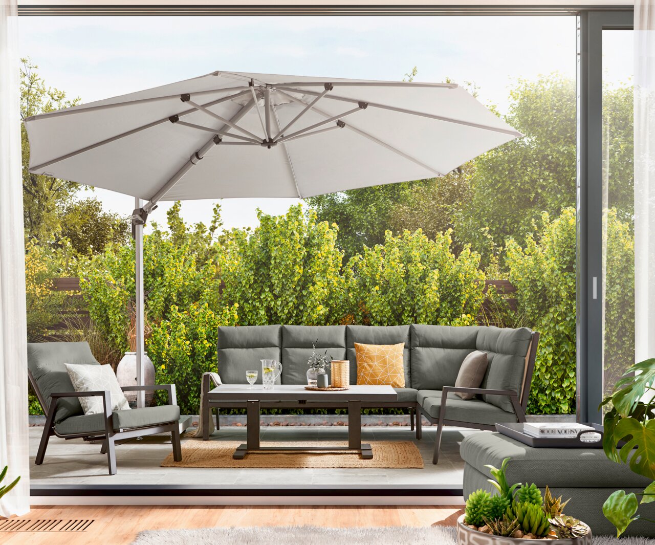 Amatio Pro Gartensessel LUZERN PLUS Gartenlounge-Set mit grauen Polstern und einem großen Sonnenschirm, aus der Perspektive einer offenen Terrassentür fotografiert.
