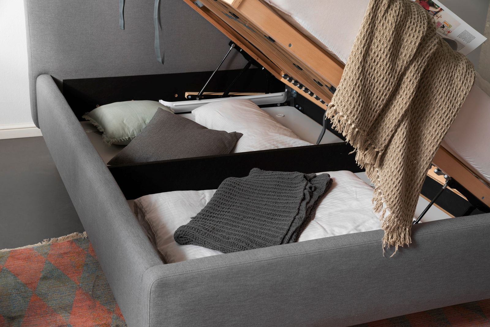 Polsterbett mit Stauraum, seitliche Perspektive, geöffnet mit Kissen und Decken.