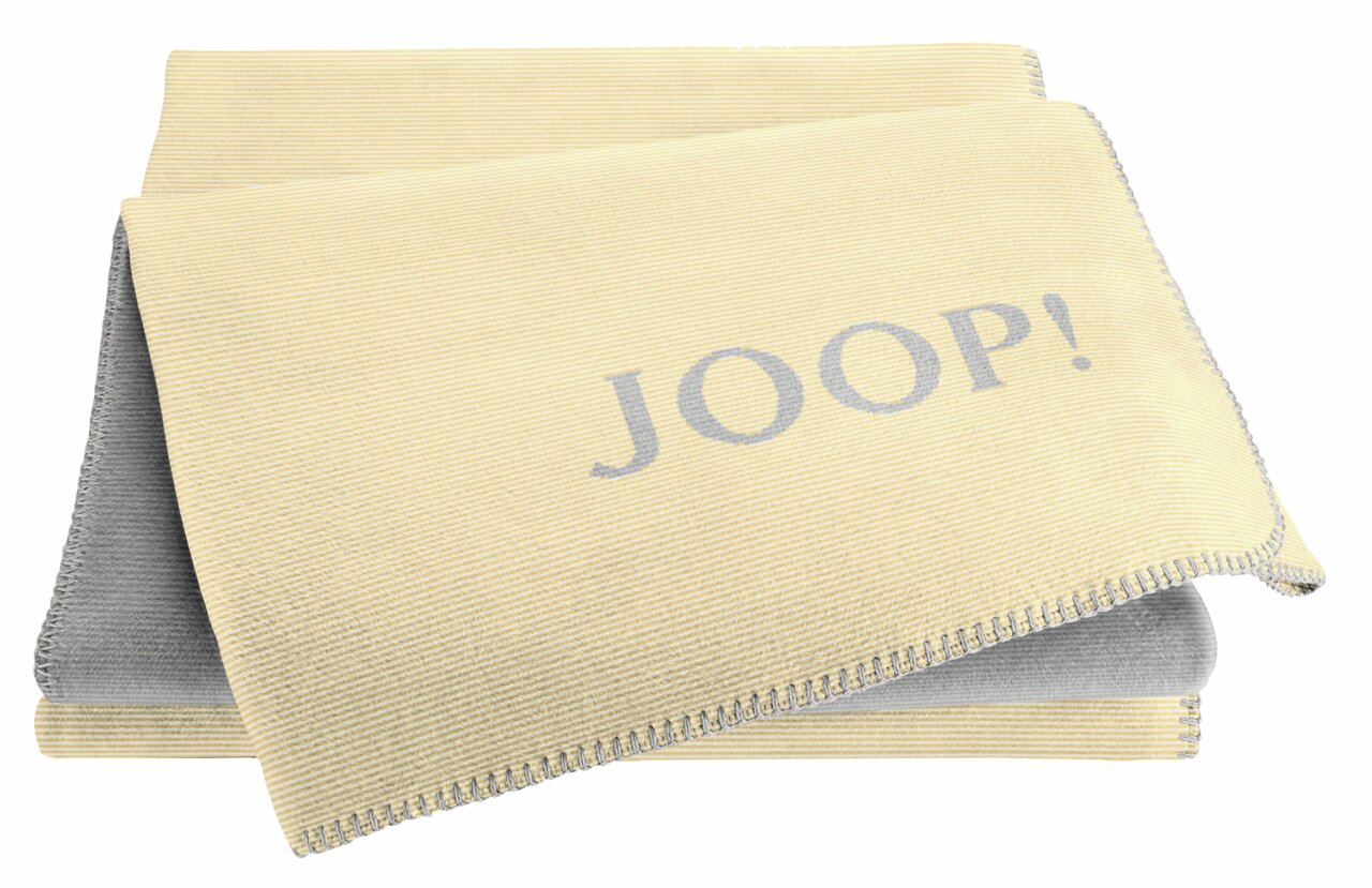 Gelbe Decke mit grauem Schriftzug 'JOOP!' in Nahaufnahme, gefaltet und von oben betrachtet.