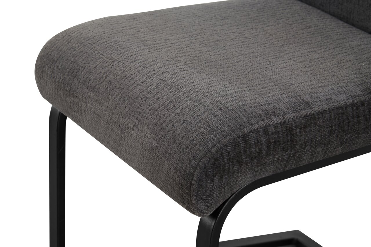 Gepolsterter Hocker mit dunkelgrauem Stoffbezug und schwarzem Metallgestell, Detailansicht aus schräger Seitenperspektive