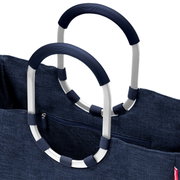Close-up vanuit een licht schuine hoek van bovenaf van een donkerblauwe stoffen tas met twee ovale, zilverkleurige aluminium handvatten met geribbelde donkerblauwe handvatbekleding en een vak met ritssluiting.