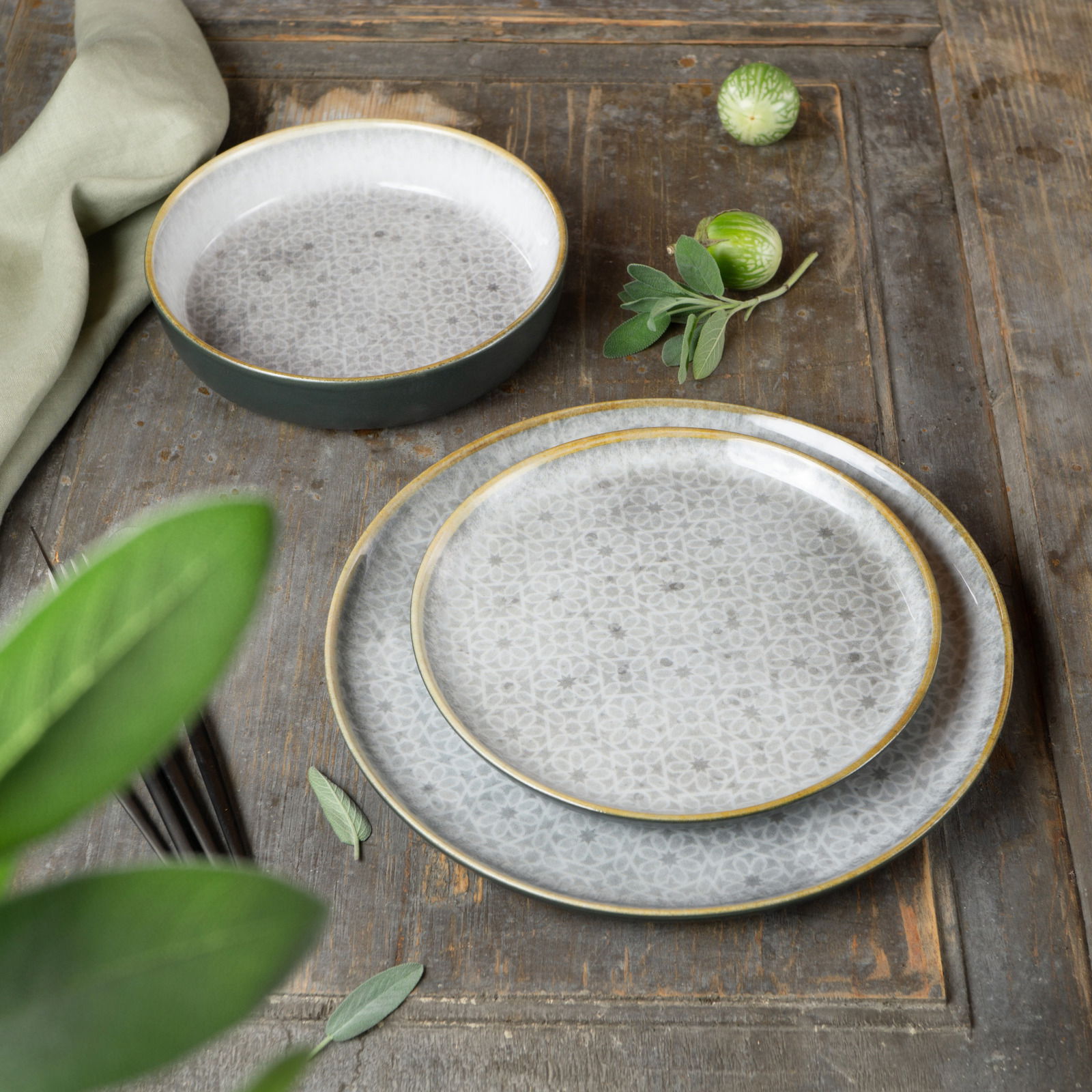 Geschirrset Terra 18-tlg. in Grau von Moritz & Moritz, bestehend aus Tellern und Schalen mit feinem Muster, auf rustikalem Holztisch von oben fotografiert.