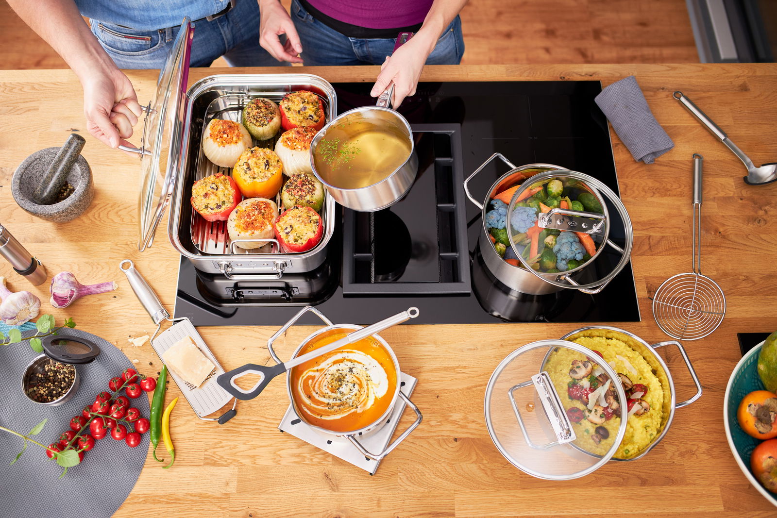 Vogelperspektive auf ein 4-teiliges Topfset auf einem Herd, gefüllt mit verschiedenen Gerichten wie gefüllten Paprika, Gemüsesuppe und gedünstetem Gemüse.