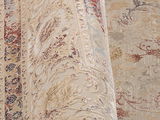 Nahaufnahme eines Orientteppichs mit floralen Mustern in Beige, Rot und Blau, perspektivisch von der Seite aufgenommen.