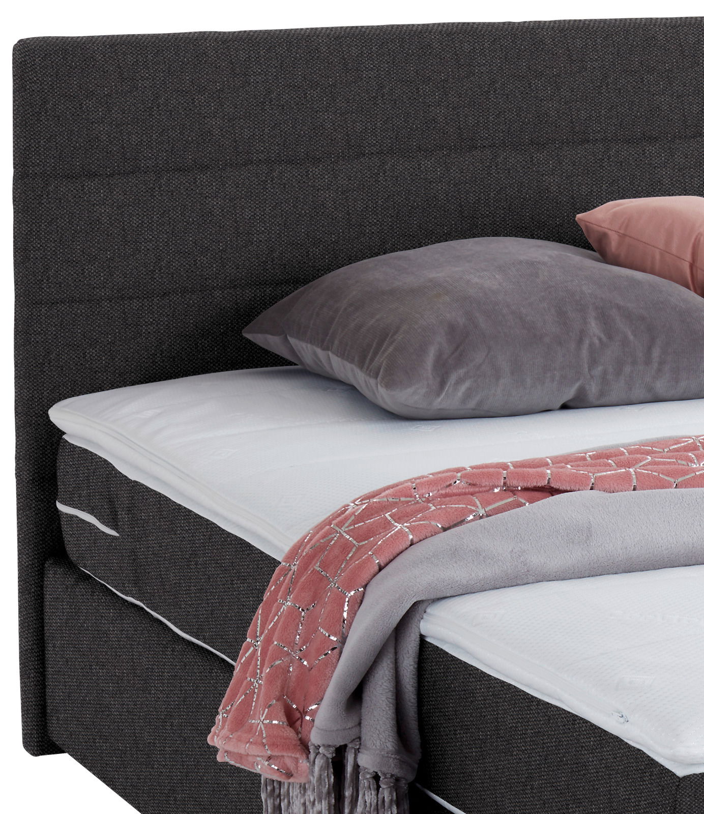 Nahaufnahme eines Boxspringbetts mit grauem Kopfteil, grauem Kissen und rosa Decke, seitliche Perspektive