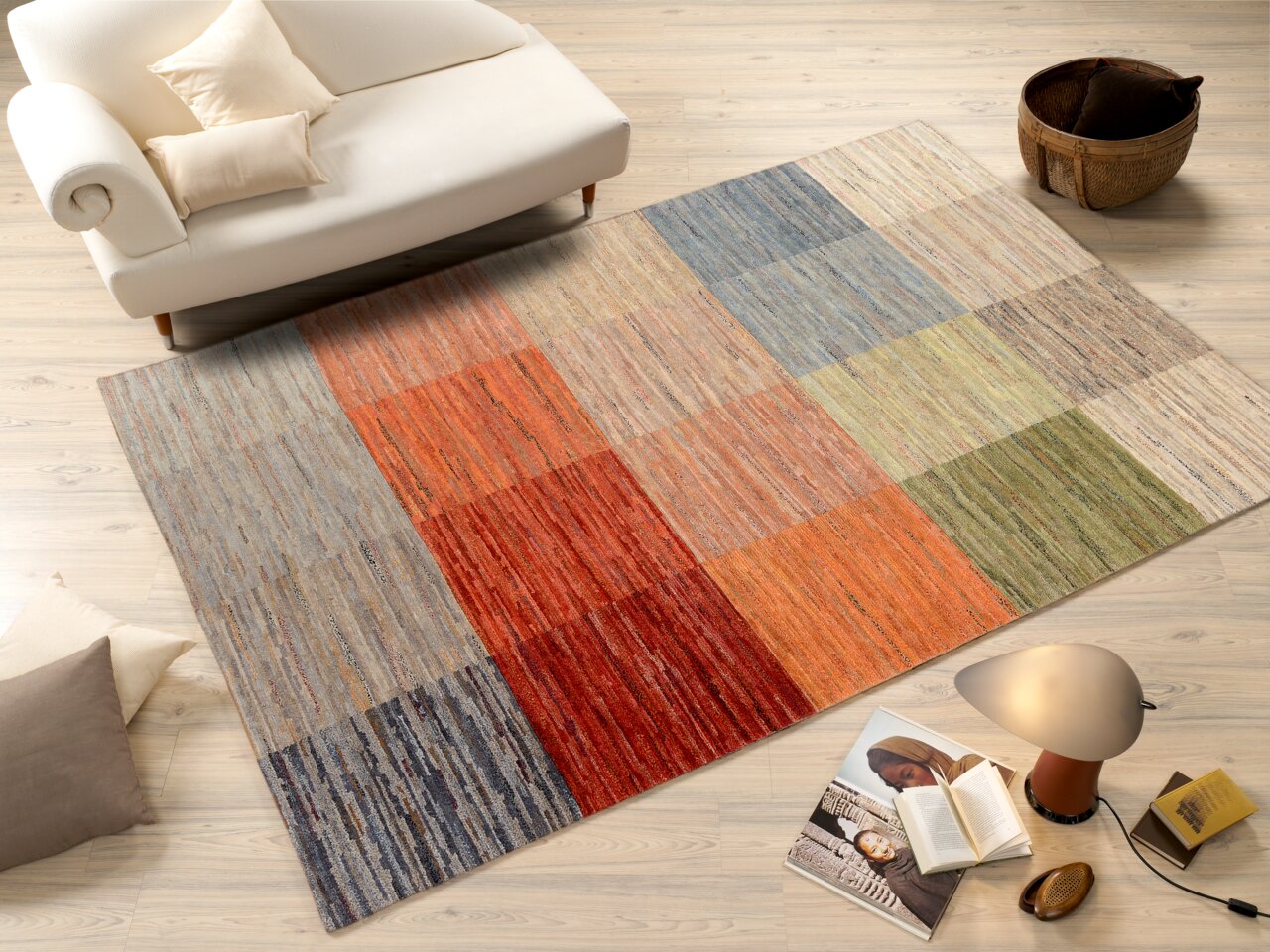 Bunte Wollteppich mit quadratischem Muster in verschiedenen Farben, auf einem hellen Holzboden neben einem weißen Sofa und einem Korb, aus der Vogelperspektive betrachtet.