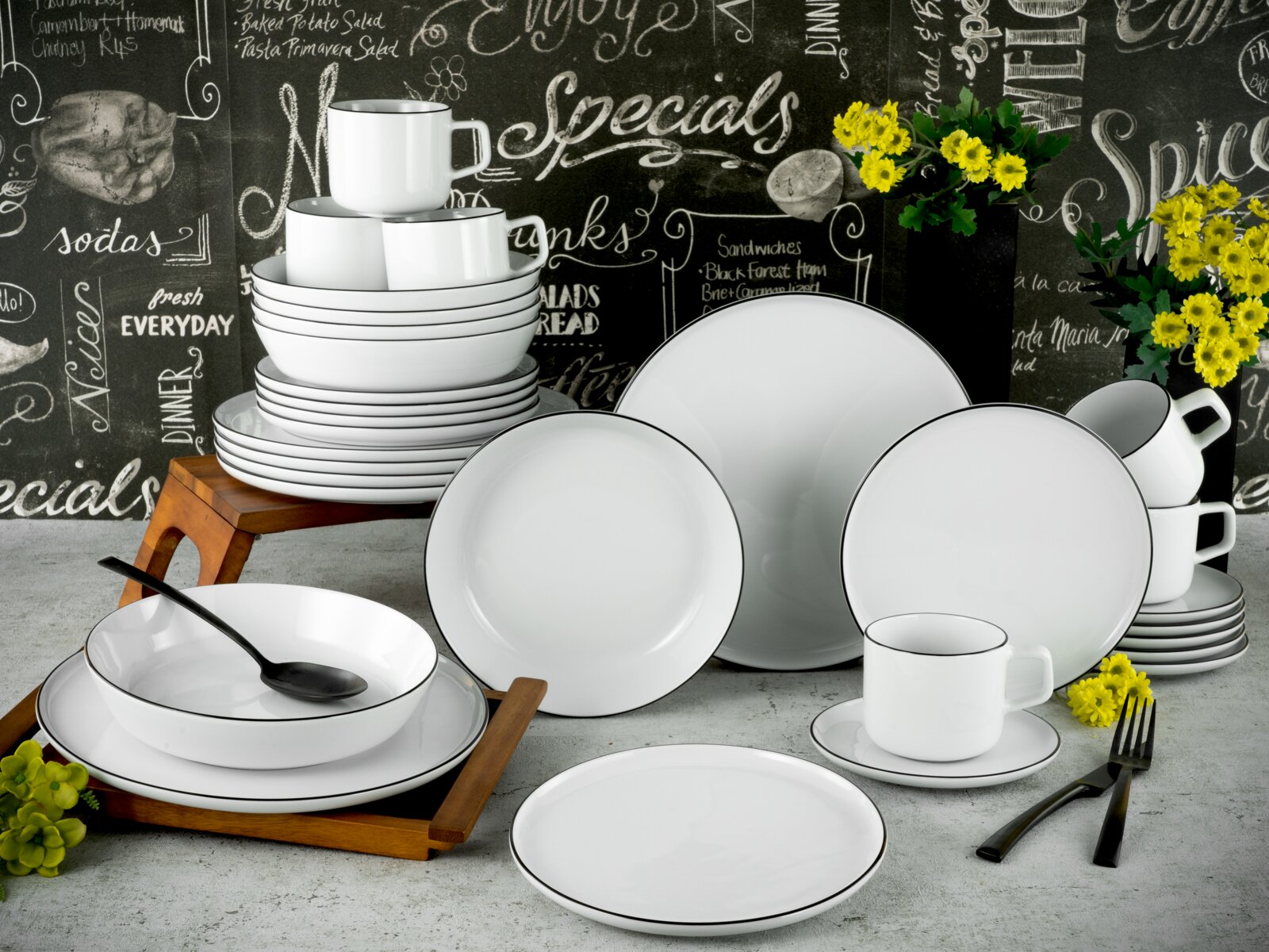 Creatable Kombiservice 30-tlg CHEF COLLECTION Weißes Porzellan-Geschirrset mit schwarzem Rand (Teller, Schalen und Tassen) dekorativ arrangiert auf Tisch vor Tafelwand, perspektivisch in frontaler leicht schräger Ansicht.