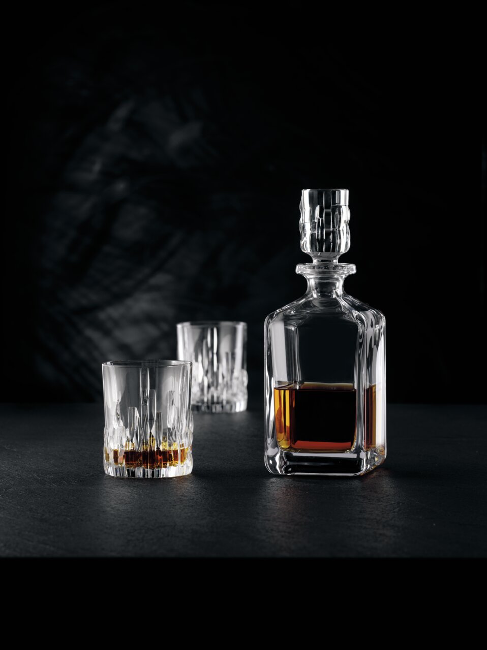 Elegante Whiskybecher und Karaffe aus Kristallglas, gefüllt mit Whisky, auf schwarzem Hintergrund. Perspektive von vorne.