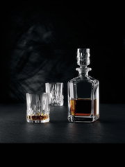 Elegante Whiskybecher und Karaffe aus Kristallglas, gefüllt mit Whisky, auf schwarzem Hintergrund. Perspektive von vorne.