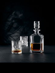 Elegante Whiskybecher und Karaffe aus Kristallglas, gefüllt mit Whisky, auf schwarzem Hintergrund. Perspektive von vorne.