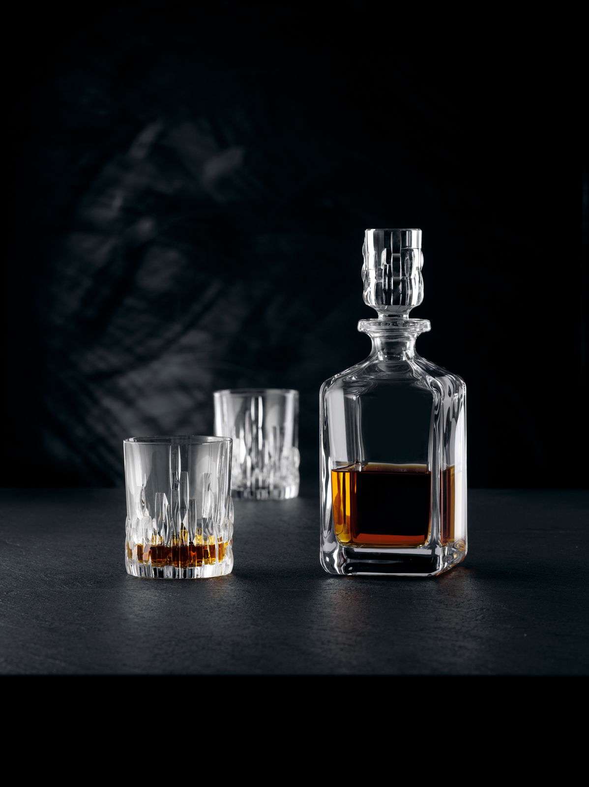 Elegante Whiskybecher und Karaffe aus Kristallglas, gefüllt mit Whisky, auf schwarzem Hintergrund. Perspektive von vorne.