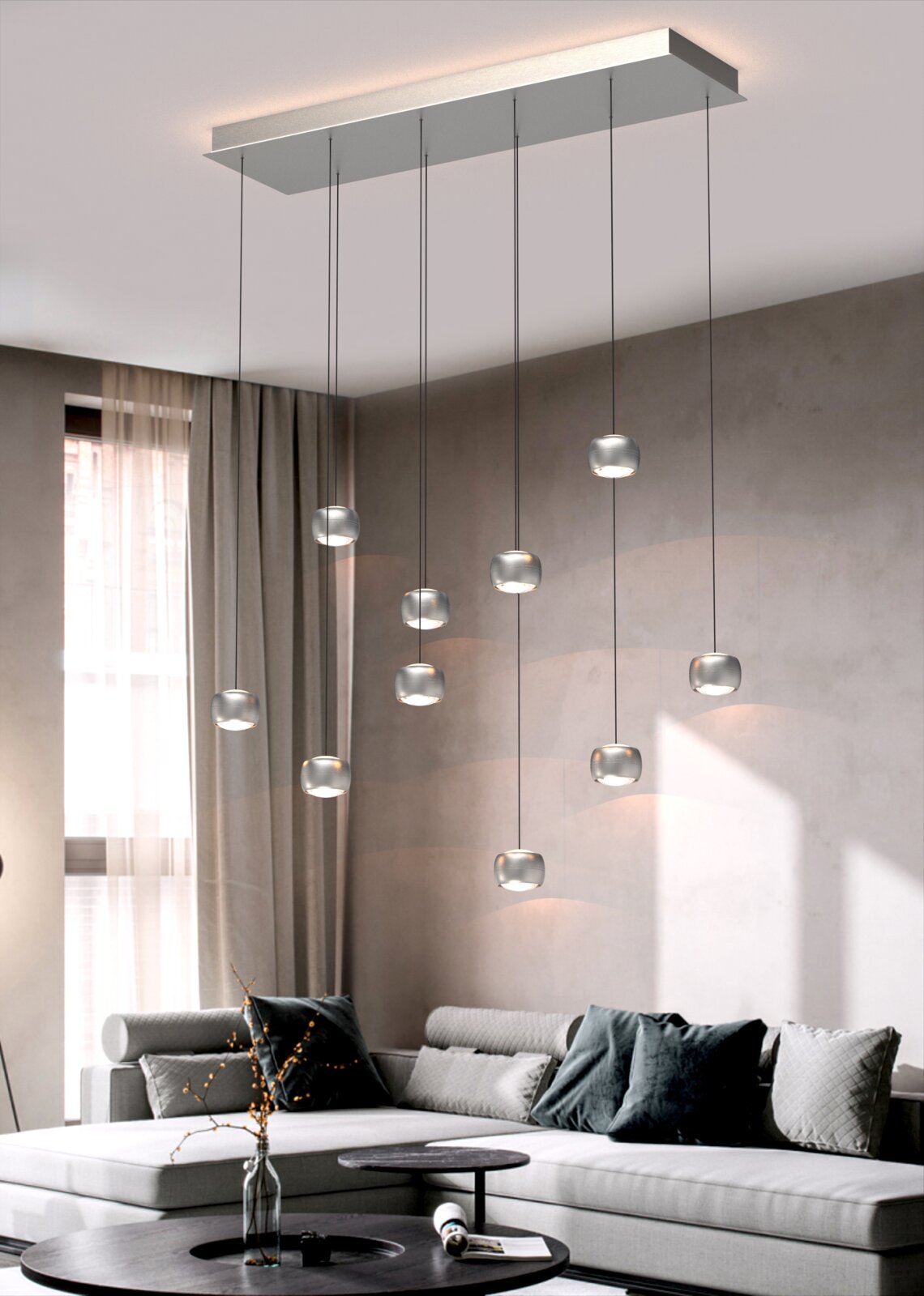 Moderne LED-hanglamp met meerdere glazen bollen, hangend aan een rechthoekige plafondbeugel, in een stijlvolle woonkamer met een grijze bank en decoratieve kussens. Aanzicht van onderaf.