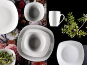 Weißes, modernes Geschirr-Set mit quadratischen Tellern, Schalen und einer Tasse auf schwarzem und floralem Hintergrund, dekoriert mit grünen Zweigen, Draufsicht (Flatlay)