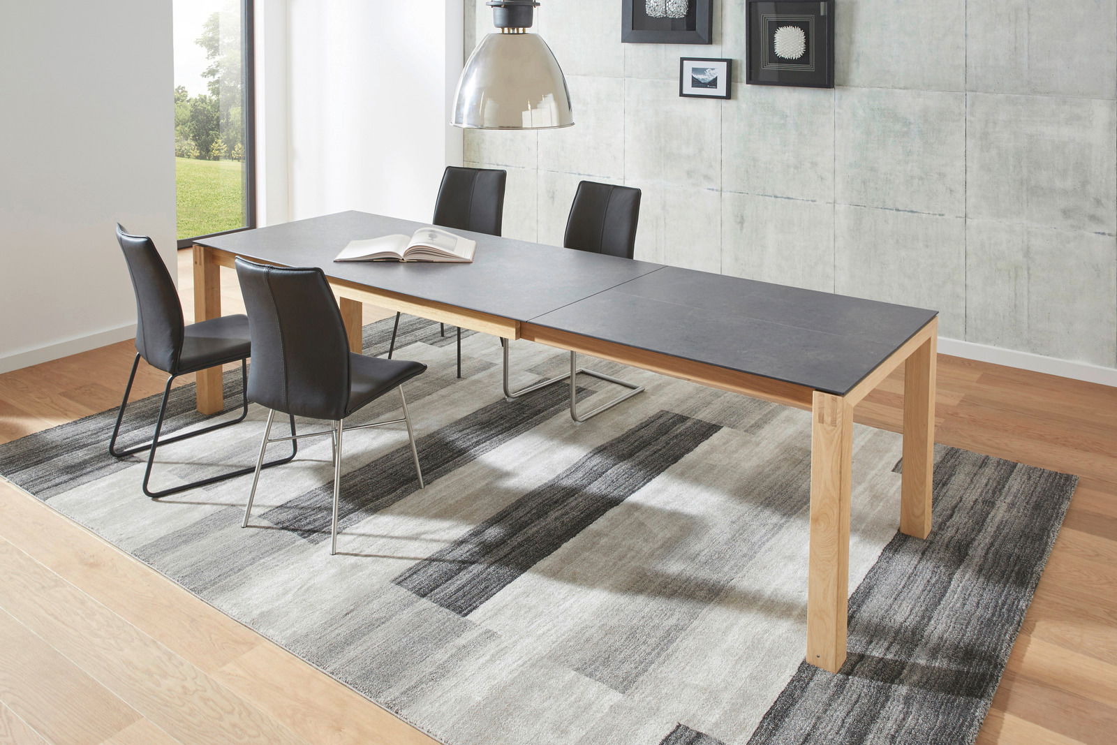 Moderner Esstisch mit schwarzer Tischplatte und Holzbeinen, umgeben von vier schwarzen Stühlen, in einem hellen Raum mit Teppich und Wanddekorationen. Perspektive: seitlich.