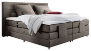Boxspringbett in seitlicher Perspektive mit grauem Stoffbezug, zwei großen Kissen und einer weißen Decke.