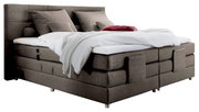 Boxspringbed in zijaanzicht met een grijze stoffen bekleding, twee grote kussens en een wit dekbed.