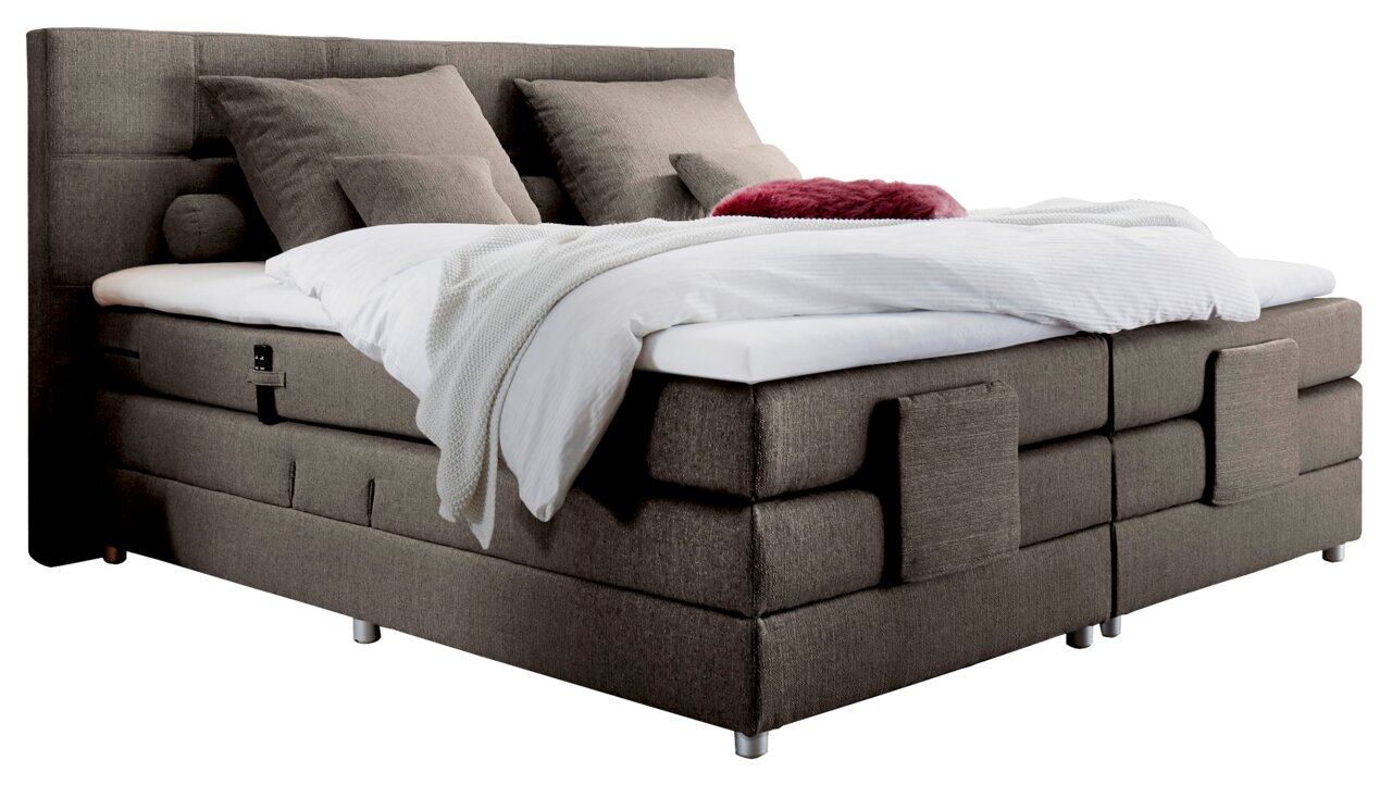 Boxspringbed in zijaanzicht met een grijze stoffen bekleding, twee grote kussens en een wit dekbed.