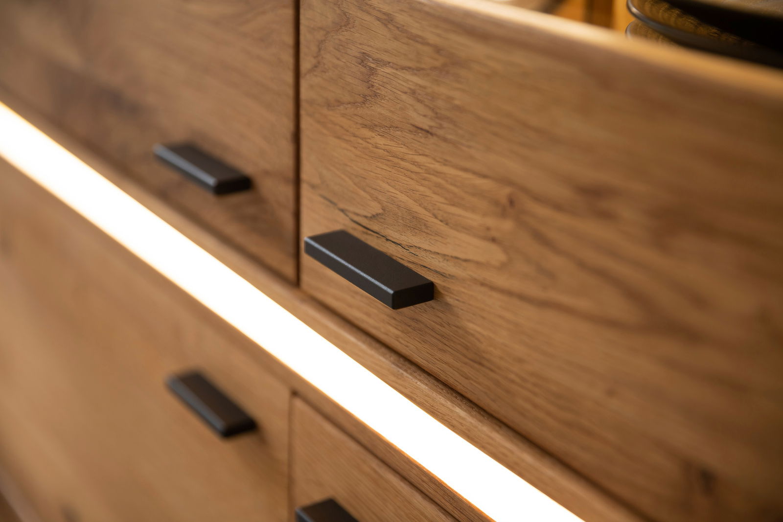 Nahaufnahme eines Highboards der Serie COMO von Zurbrüggen mit Holzmaserung und modernen schwarzen Griffen, seitliche Perspektive.