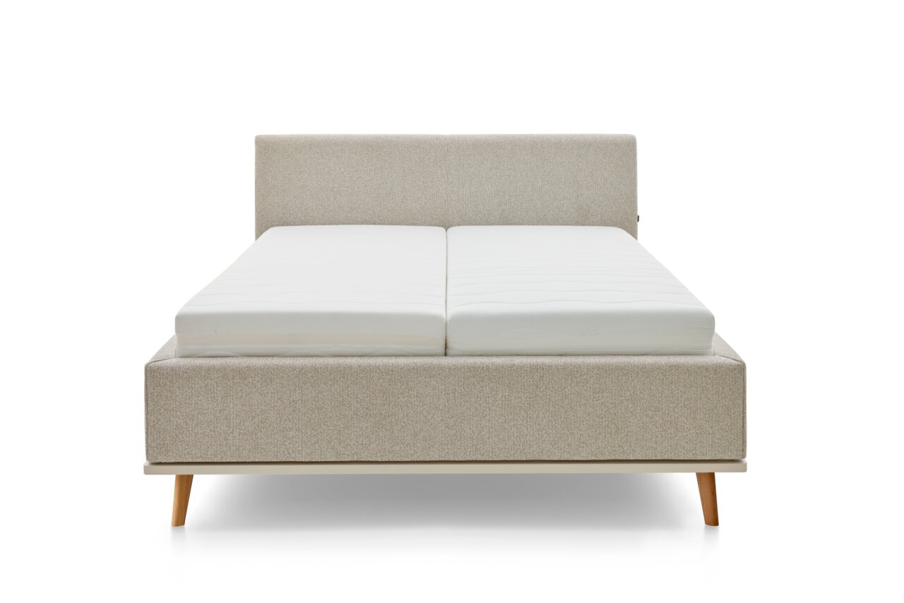 Vooraanzicht van een modern gestoffeerd bed met een lichte stoffen bekleding en houten poten.