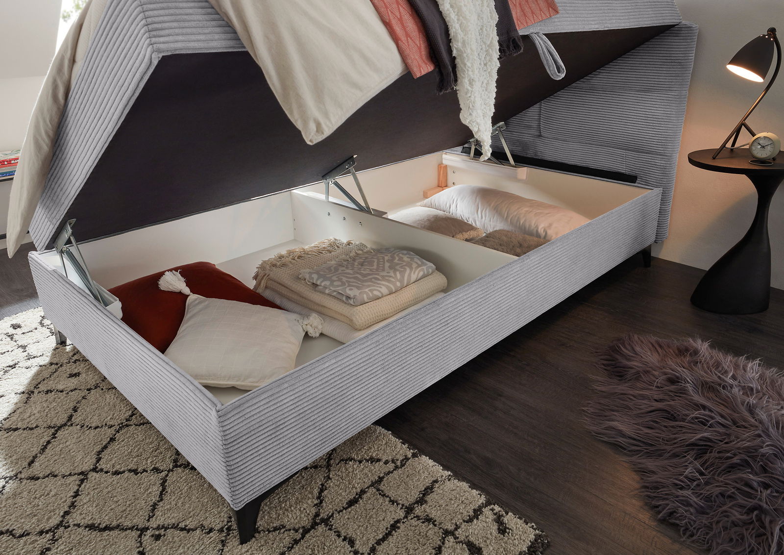 Boxbett mit geöffnetem Stauraum, gefüllt mit Kissen und Decken, aus seitlicher Perspektive.