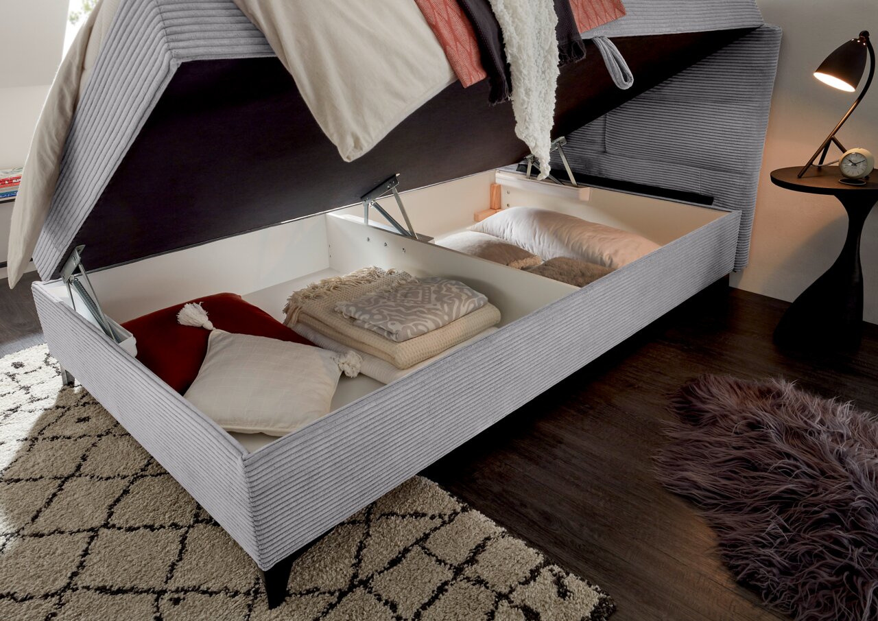 Boxbett mit geöffnetem Stauraum, gefüllt mit Kissen und Decken, aus seitlicher Perspektive.