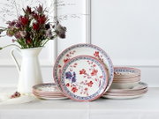 Blumenporzellan-Geschirrset mit Tellern und Schalen in Weiß mit rotem und blauem Blütendekor, seitlich auf einem Tisch arrangiert, Frontansicht leicht schräg von vorn.