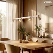 Moderne, lineare Pendelleuchte in Weiß mit vier verstellbaren Spotköpfen über einem Holzesstisch in einem hellen Esszimmer; Perspektive: leicht seitliche Ansicht auf Augenhöhe.
