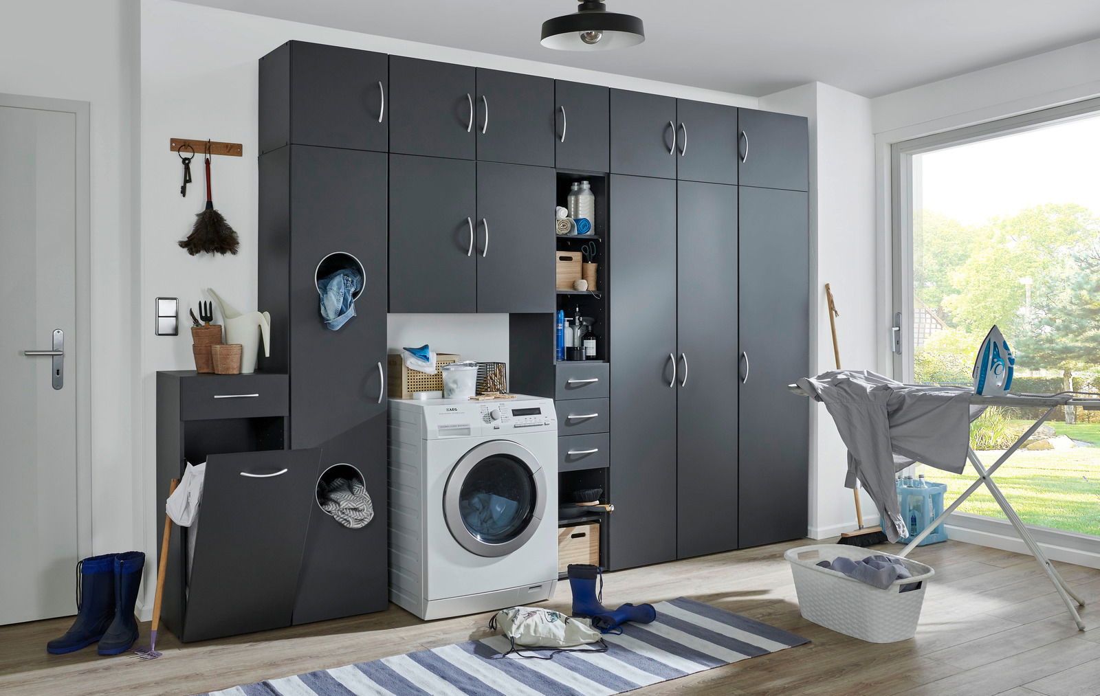Moderne Waschküche mit grauen Schränken, Waschmaschine und Bügelstation, seitliche Perspektive