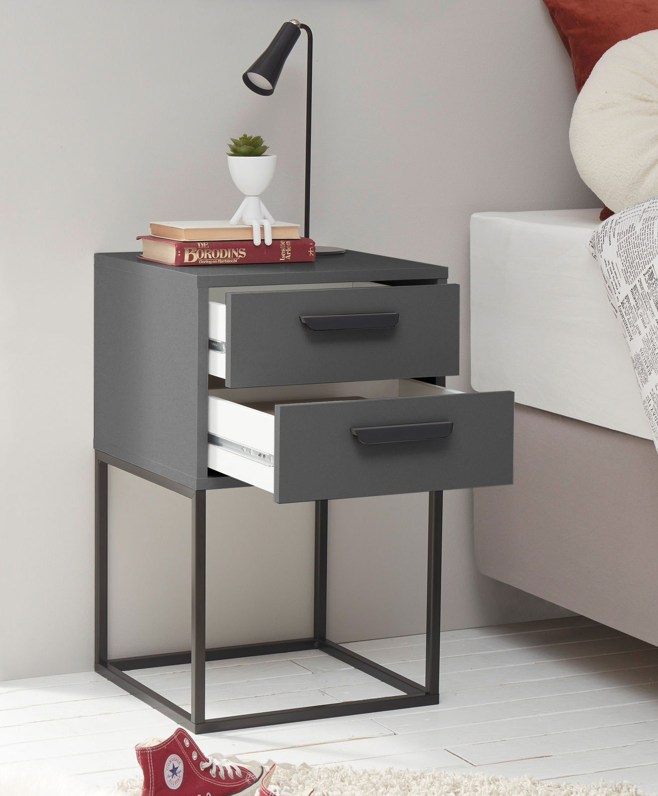Moderne Nachtkommode mit zwei offenen Schubladen, schwarzem Metallgestell und grauer Oberfläche, seitliche Perspektive.