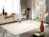 Heller Uni-Teppich in einem modernen Wohnzimmer, fotografiert aus einer leicht erhöhten Perspektive. Der Teppich liegt auf einem glänzenden Fliesenboden, umgeben von stilvollen Möbeln und Dekorationen.