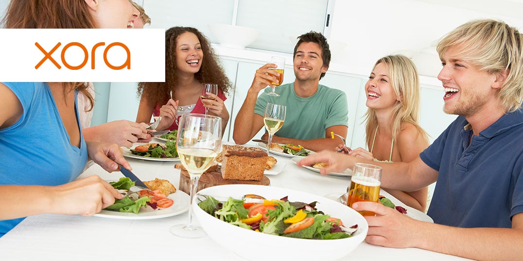 Eine fröhliche Gruppe junger Menschen isst gemeinsam an einem Tisch mit Salat, Brot und Getränken.