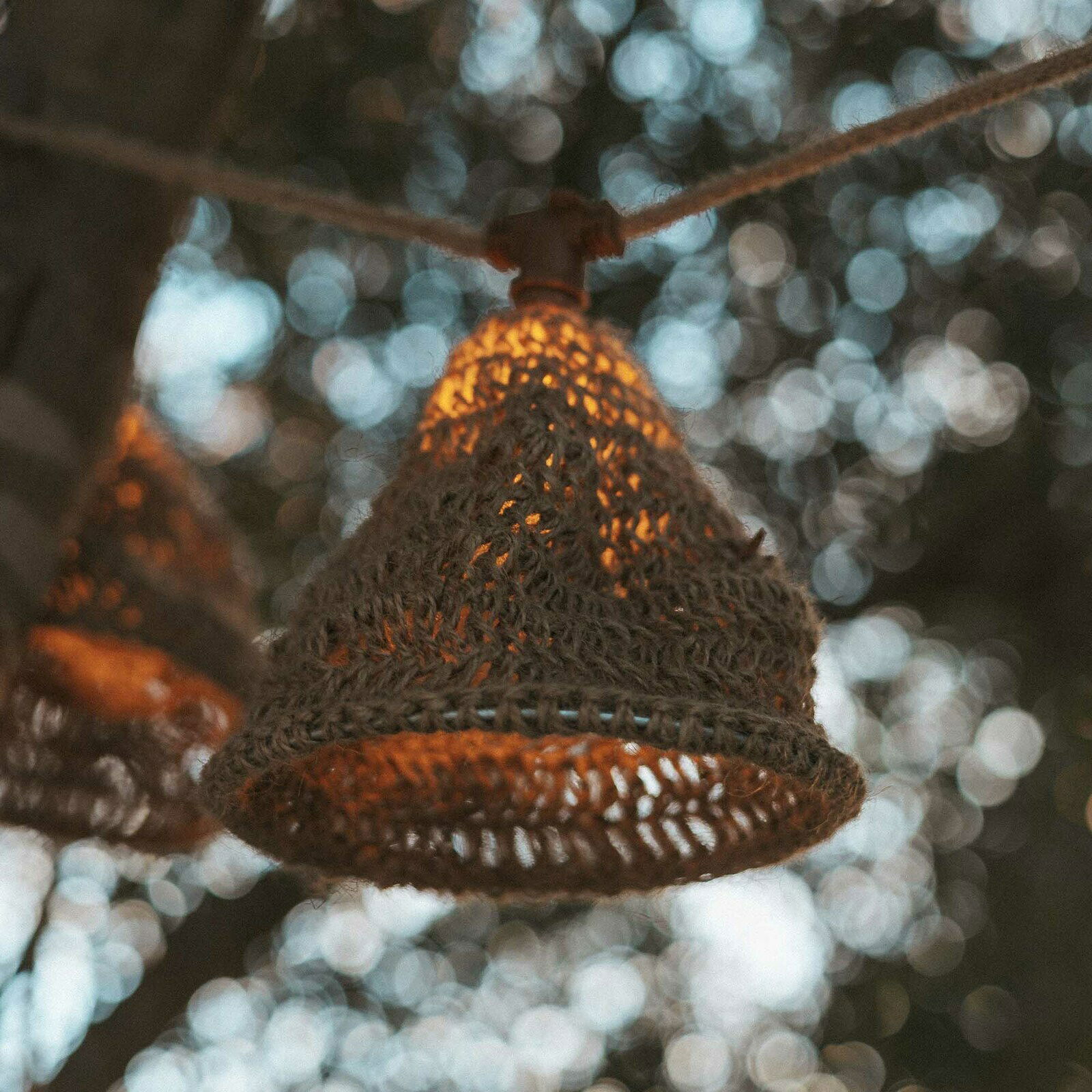 Nahaufnahme einer Outdoor-Lichterkette mit einem geflochtenen Lampenschirm, der an einem Baum hängt. Die Lichterkette leuchtet warm im Hintergrund eines unscharfen, natürlichen Umfelds.
