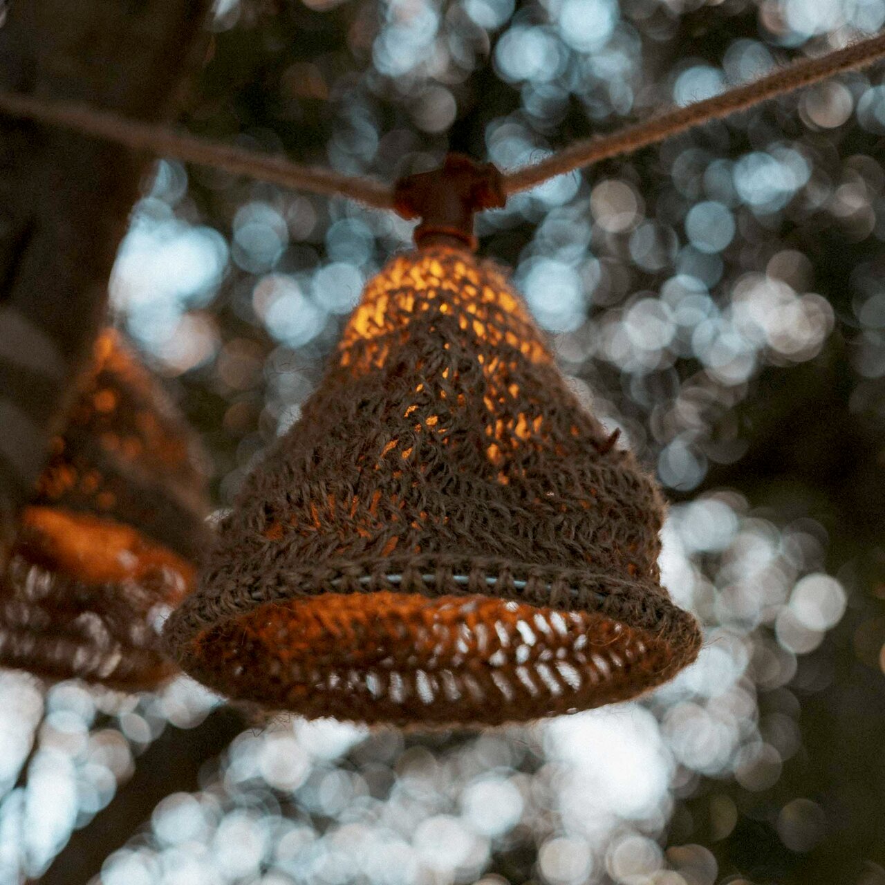 Nahaufnahme einer Outdoor-Lichterkette mit einem geflochtenen Lampenschirm, der an einem Baum hängt. Die Lichterkette leuchtet warm im Hintergrund eines unscharfen, natürlichen Umfelds.