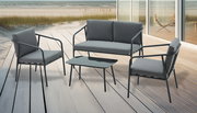 Modernes Outdoor-Lounge-Set in Anthrazit mit 2-Sitzer-Sofa, zwei Sesseln und niedrigem Couchtisch auf Holzterrasse am Strand, Perspektive: leicht erhöhte Frontansicht schräg von links