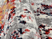 Nahaufnahme eines Designer-Teppichs mit abstraktem Muster in Grau, Rot, Gelb und Blau. Die Perspektive zeigt eine seitliche Ansicht der Textur und Farben.