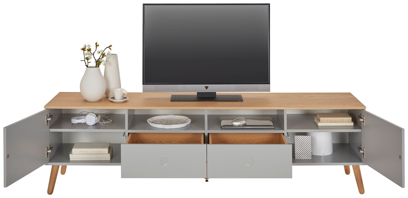 Modernes TV-Board mit Holzoberfläche und grauen Schubladen, frontal fotografiert. Dekoriert mit Vasen, Tasse und Kopfhörern.