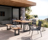 Moderner Gartentisch aus Holz mit Metallgestell auf einer Terrasse, umgeben von Stühlen und einer Bank, mit Blick auf die Natur.