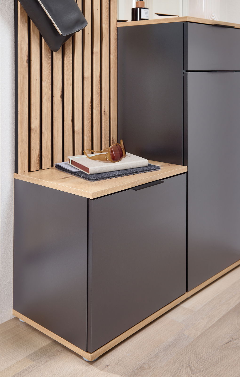 Kompaktgarderobe mit modernem Design, bestehend aus einem dunklen Schrank mit Holzdetails und einer Ablagefläche, seitliche Perspektive