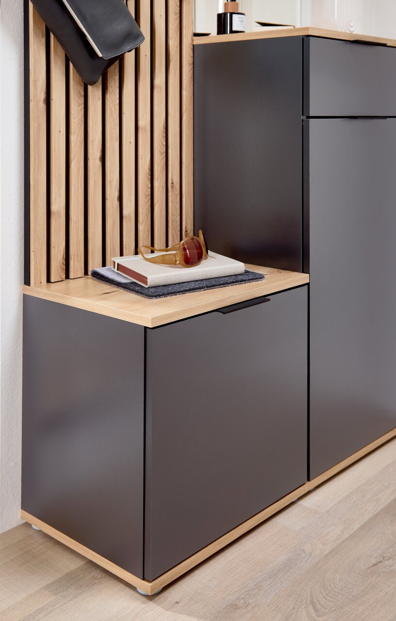 Kompaktgarderobe mit modernem Design, bestehend aus einem dunklen Schrank mit Holzdetails und einer Ablagefläche, seitliche Perspektive