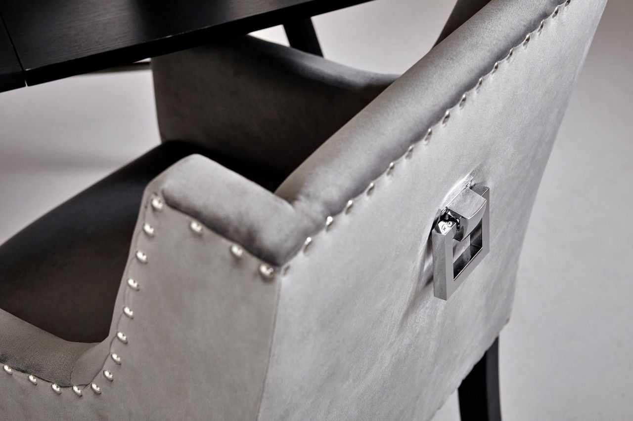 Detailansicht eines grauen Stuhls mit Nietenverzierung und Metallgriff an der Rückenlehne.