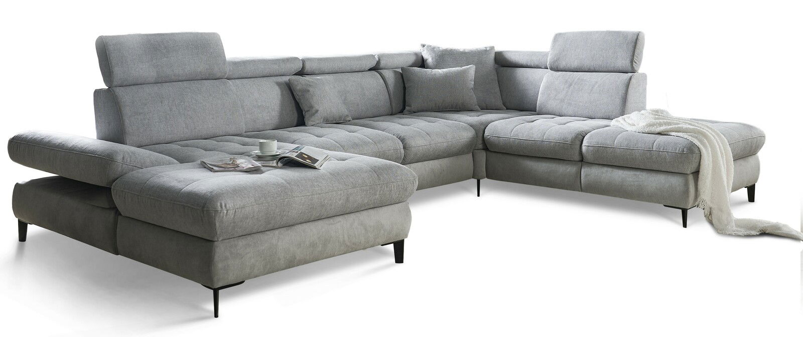 Graues Ecksofa mit verstellbaren Kopfstützen und Kissen, von vorne links gesehen, mit einer Tasse und Zeitschrift auf der Sitzfläche.