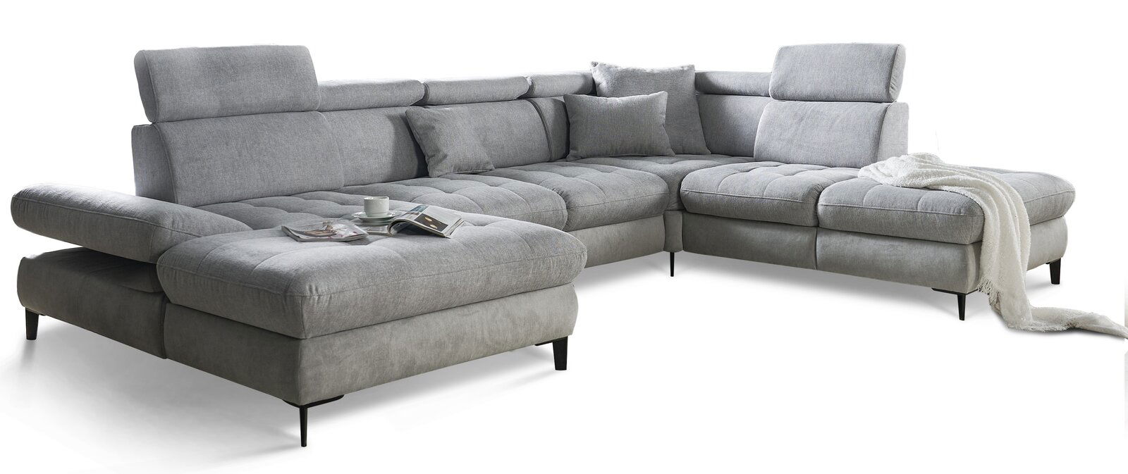 Graues Ecksofa mit verstellbaren Kopfstützen und Kissen, von vorne links gesehen, mit einer Tasse und Zeitschrift auf der Sitzfläche.
