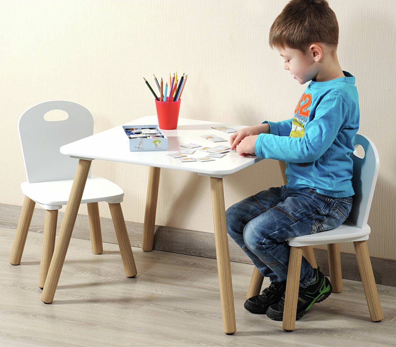 Kindertisch mit zwei weißen Stühlen, ein Kind sitzt und spielt am Tisch, seitliche Perspektive