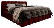 Gestoffeerd bedframe in rood met doorgestikt hoofdeinde, gezien vanaf de zijkant, versierd met een grijze deken en een geruite sprei.