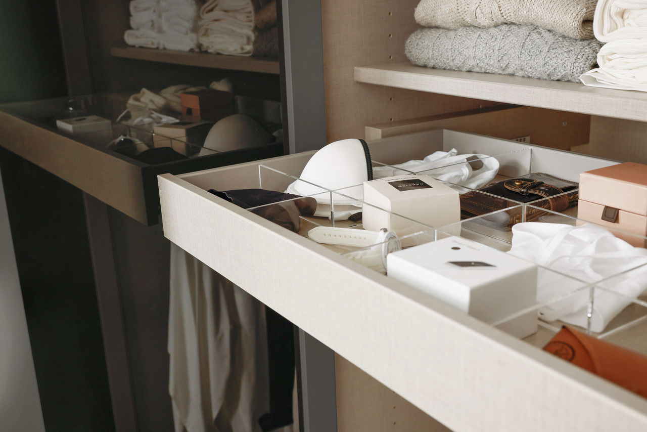 Nahaufnahme eines offenen Schubladeneinsatzes in einem sechstürigen Drehtürenschrank, gefüllt mit Kleidung und Accessoires, von der Seite betrachtet.