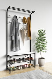 Moderner Garderobenständer aus schwarzem Metall mit weißer Rückwand, Hutablage, mehreren Haken, Sitzbank und zweistöckigem Schuhregal, frontal in leichter Schrägansicht von links fotografiert; daran hängen Mantel, Schal und Regenschirm in einem hellen Flu