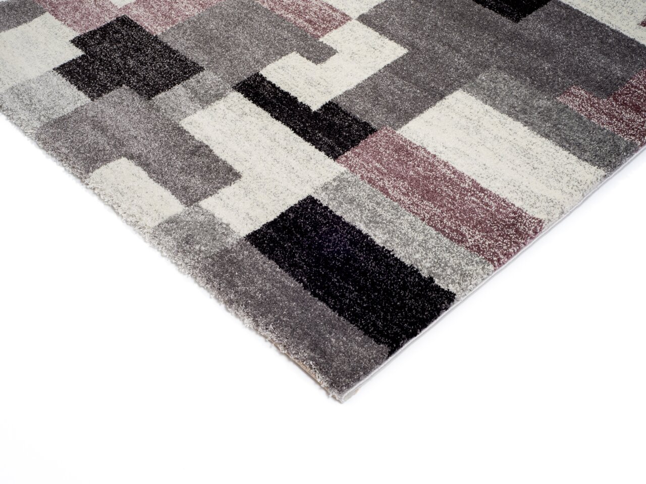 Ecke eines Frisé-Teppichs mit geometrischem Muster in Grau-, Schwarz- und Violetttönen, von oben fotografiert.